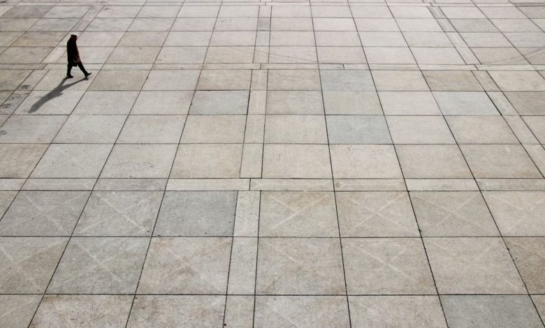 مرد تنها روی سنگ‌فرش‌های بزرگ و خالی راه می‌رود